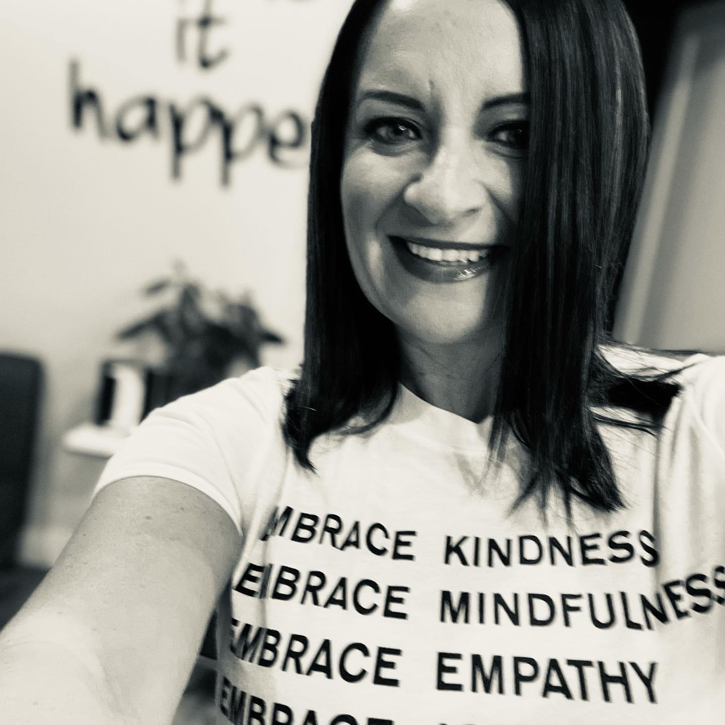 Tara Allen smiling in a shirt printed with messages about embracing kindness, mindfulness, and empathy