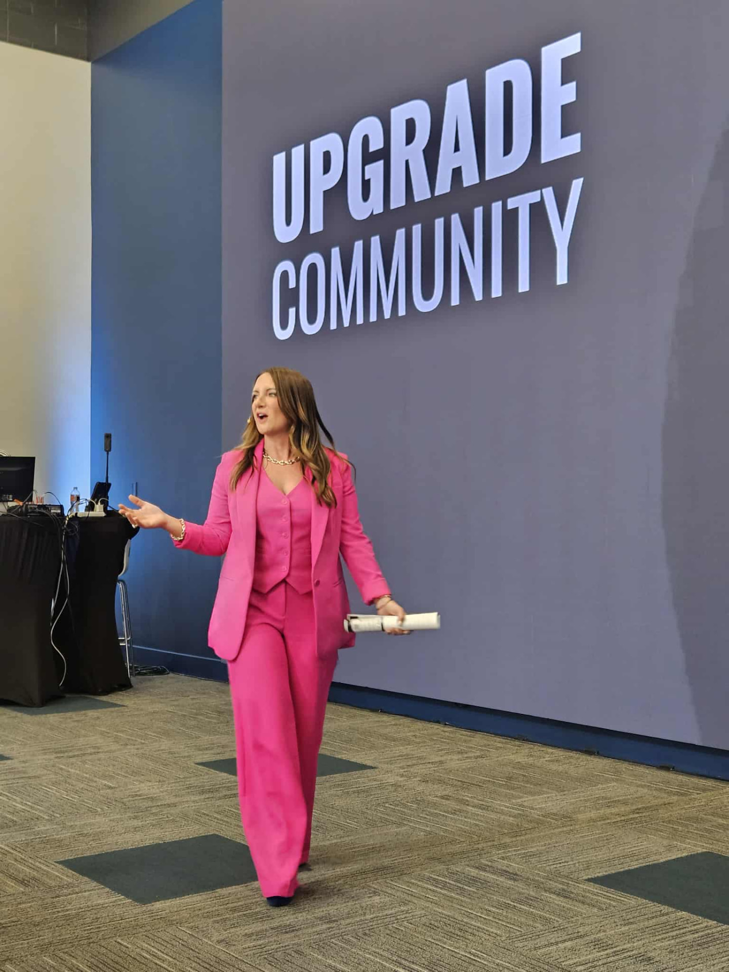 Tara Allen speaking on stage in front of an Upgrade Community backdrop