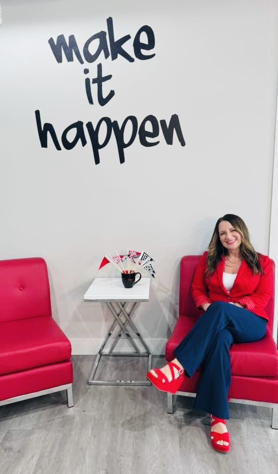 Tara Allen seated in a bright red chair beneath a wall mural reading 'make it happen'